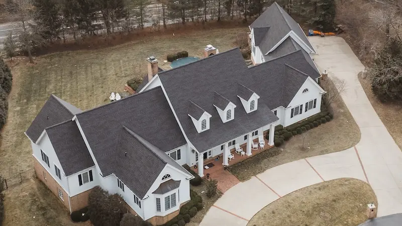 Aerial drone view of luxury white colonial home with storm damage roof replacement by Cardinal Contractors serving Kansas City and St. Louis Missouri