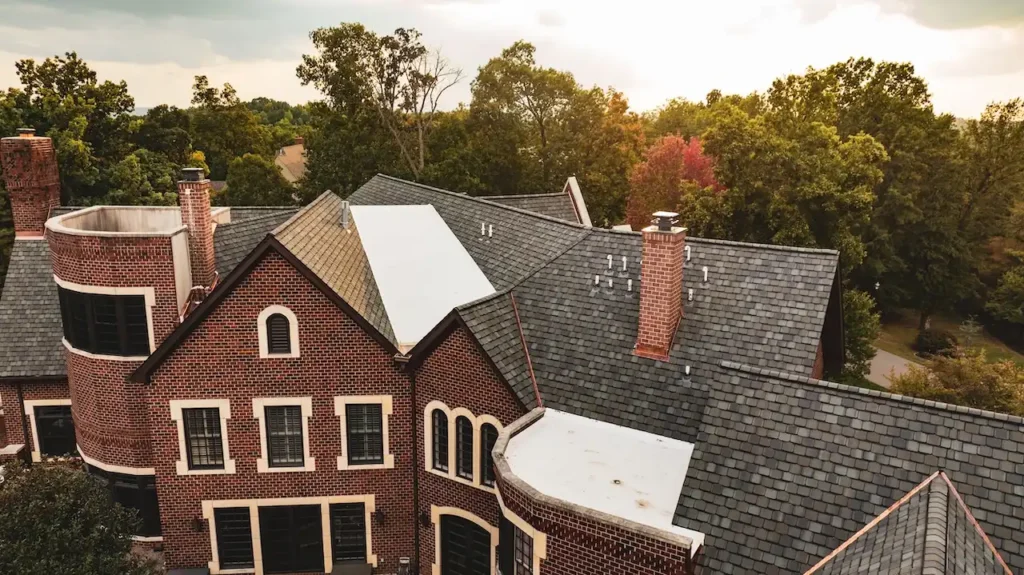 Close aerial view of luxury brick Tudor manor with slate style shingles and flat roof sections assessed for insurance claim roofing by Cardinal Contractors in St. Louis MO